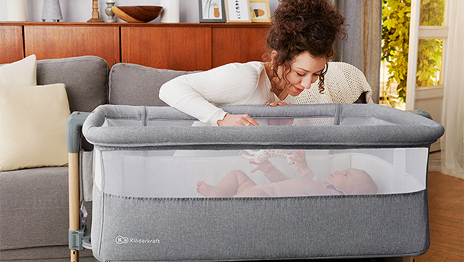In der Wohnung beugt sich die Mutter mit einem Lächeln über das winzige Baby, das spielend im Kinderkraft-Bettchen liegt.
