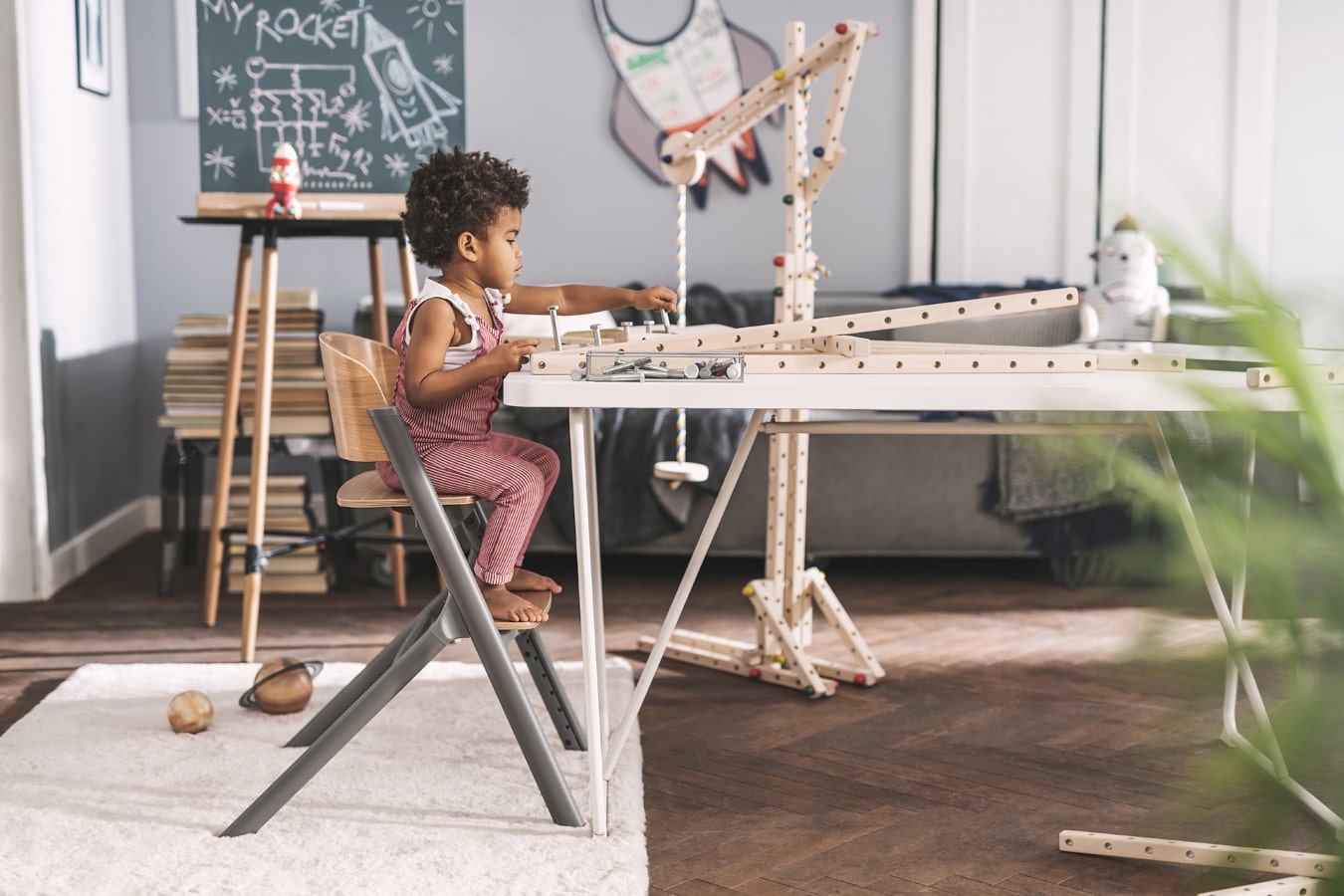 Ein kleiner Junge mit schwarzen Haaren baut eine Holzkonstruktion, er sitzt sehr konzentriert im  LIVY-Kinderhochstuhl von Kinderkraft